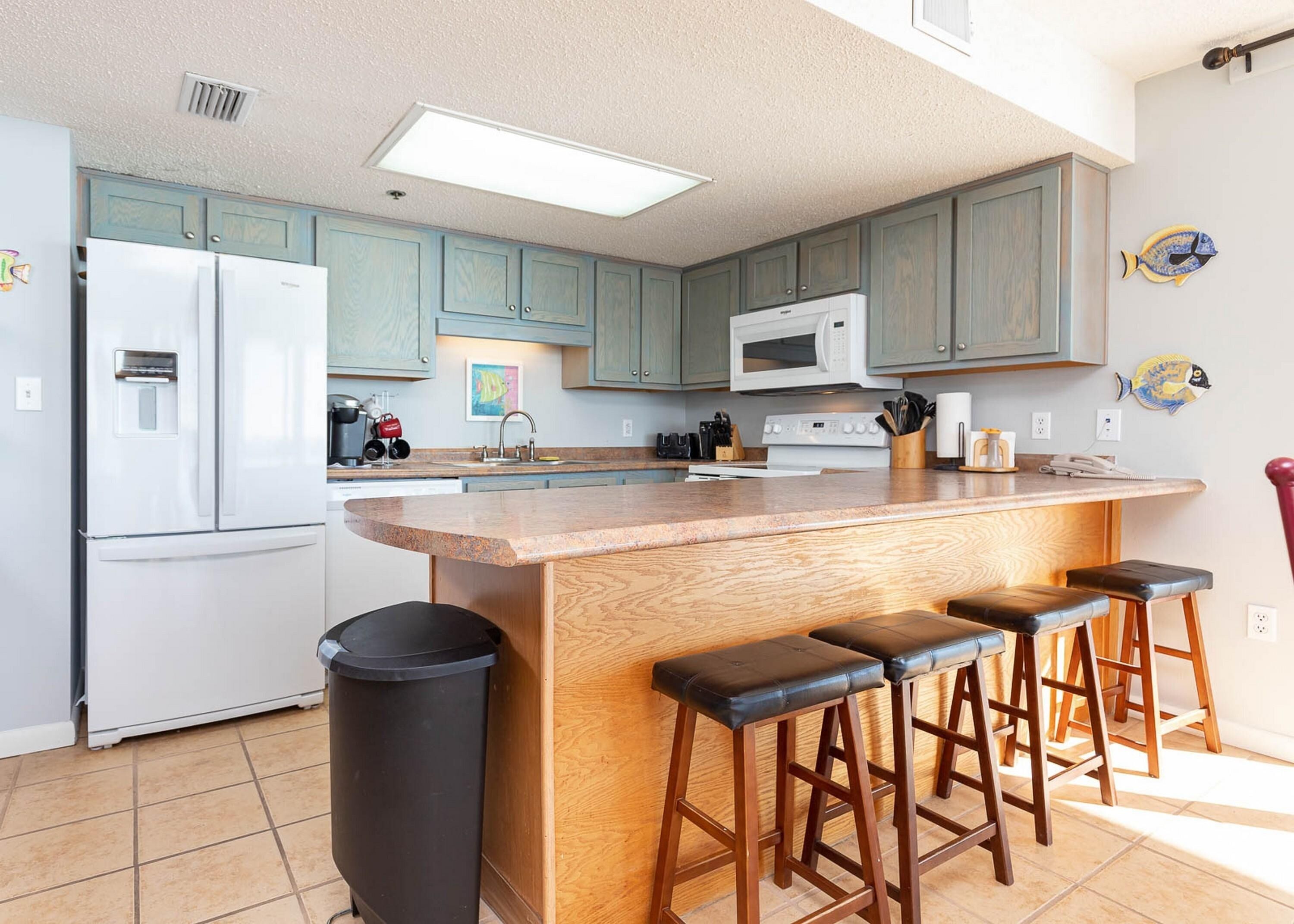 A kitchen with a central island, bar stools, a microwave, and a refrigerator.