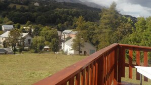 Une terrasse en bois offrant une vue sur un paysage rural, avec des maisons et des arbres, sous un ciel nuageux.