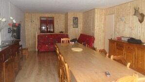 Un espace repas comprenant une longue table en bois, un canapé rouge à motifs et des meubles de rangement en bois.