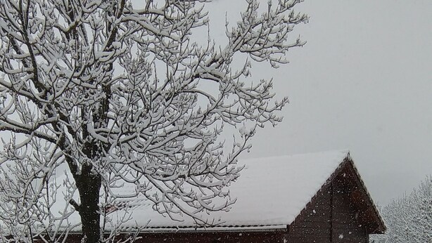 Une grange en bois, dont le toit est recouvert de neige, et un pont en bois qui y mène.