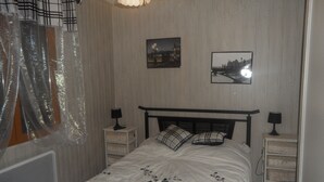Une chambre à coucher comprenant un lit, deux tables de chevet, un radiateur et deux tableaux accrochés au mur.