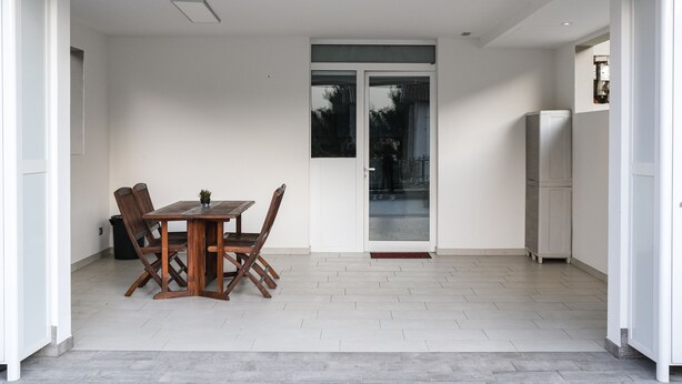 A modern kitchen with a dining area, featuring a wooden table and chairs, a refrigerator, and a sliding glass door leading to an outdoor area. - Brand New 2-bed Apartment With Patio (Endine Gaiano)