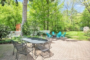 Eine Terrasse mit Tisch und Stühlen, umgeben von Bäumen und einem weißen Zaun.