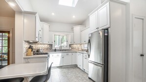 Una cocina moderna con armarios blancos, un refrigerador de acero inoxidable y una zona de comedor con mesa blanca y sillas negras.