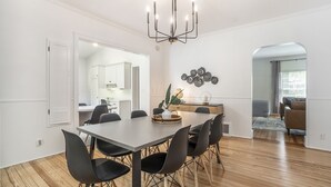 Un comedor con una mesa rectangular, sillas negras, una araña y un adorno en la pared.
