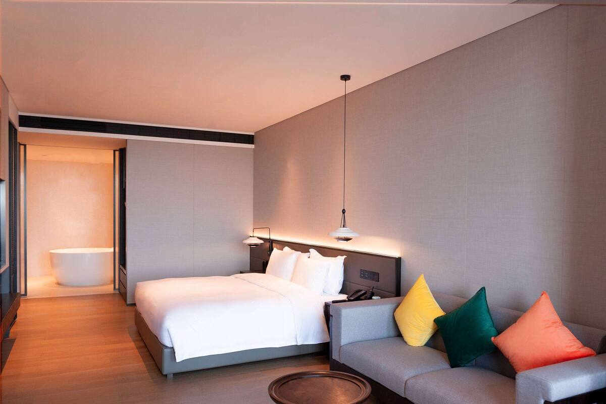 Ein modernes Hotelzimmer mit Bett, Sofa, Nachttisch und einem Badezimmer mit Badewanne.