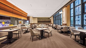 Un restaurant moderne doté de nombreuses tables et chaises, d’un bar et de grandes fenêtres offrant une vue sur la ville.
