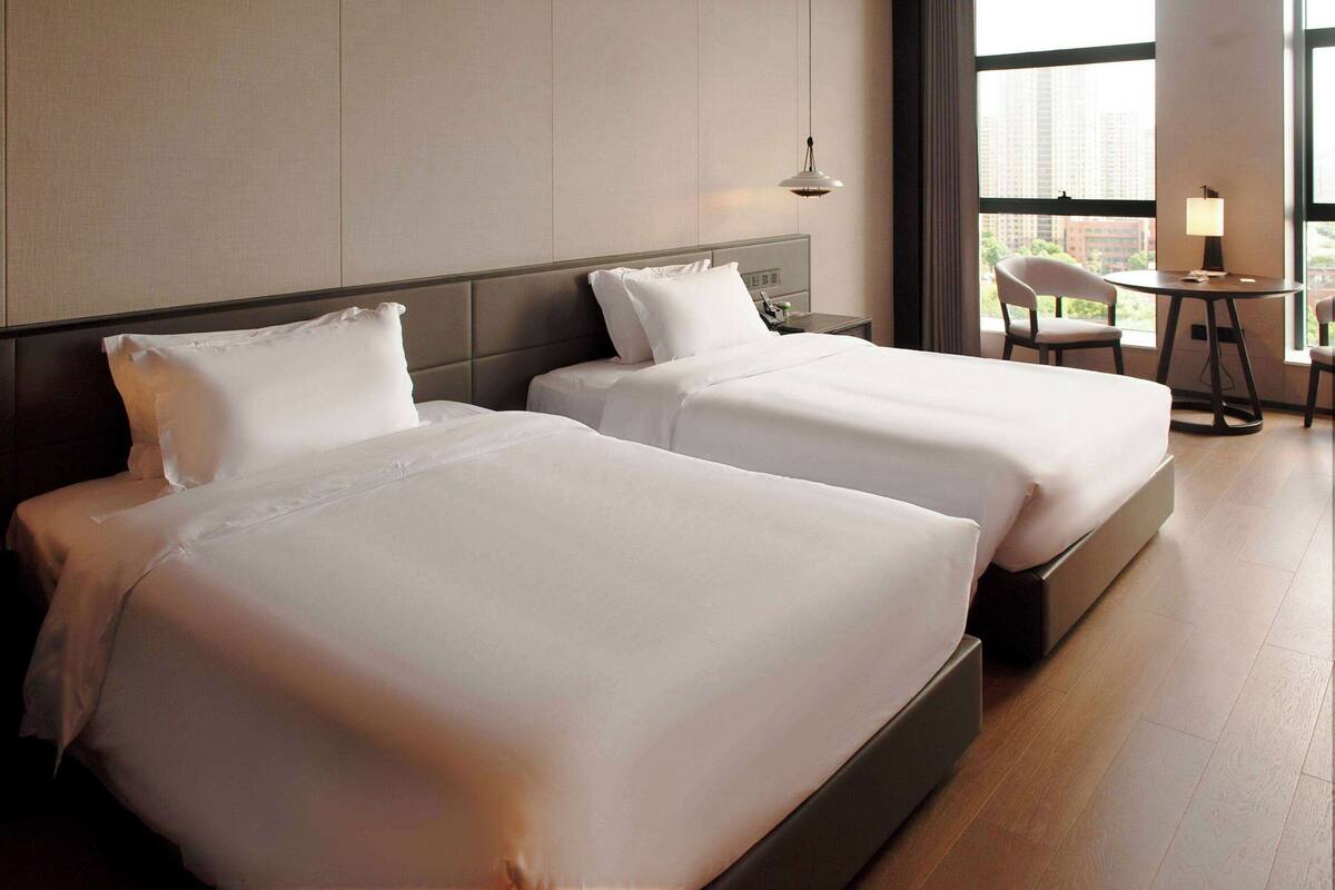 Ein Hotelzimmer mit zwei Betten, einem kleinen Tisch mit Stühlen und einem großen Fenster mit Blick auf die Stadt.