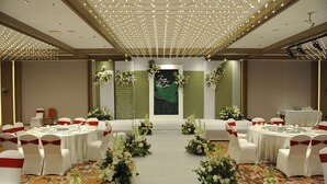 Une salle de banquet avec des tables rondes, des chaises blanches ornées de rubans rouges et des centres de table floraux.