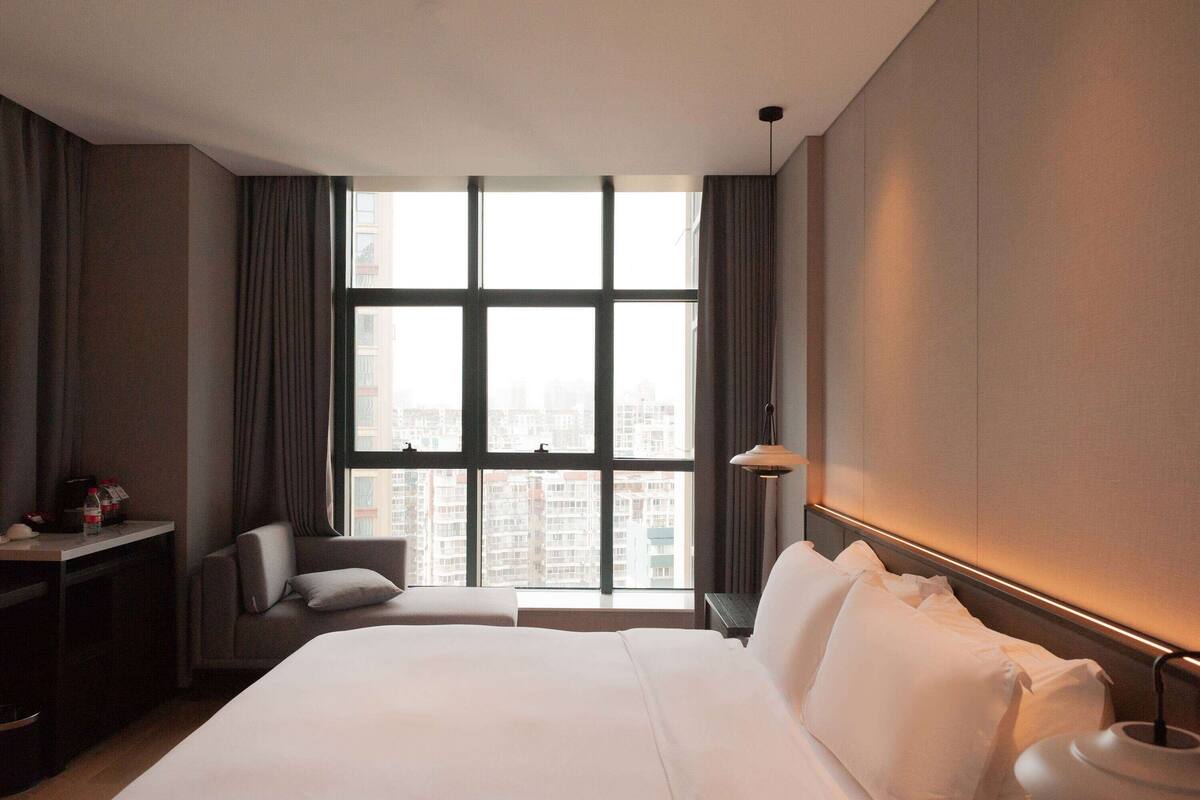 Ein Hotelzimmer mit großem Fenster, einem Bett, einem Schreibtisch und einem Stuhl.