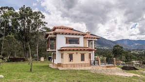 A two-story house with a tiled roof, surrounded by a grassy area and trees. - The village of San Juan (Villa de Leyva)
