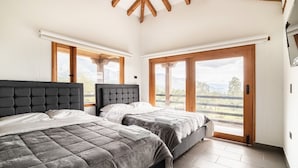 A bedroom with two beds, large windows, and a wooden ceiling. - The village of San Juan (Villa de Leyva)