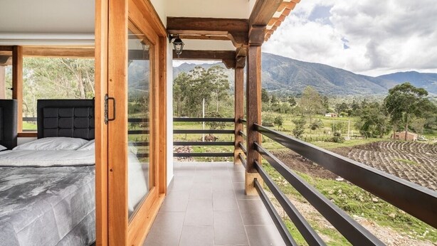 A bedroom with a large bed, a wooden balcony with a view of mountains and fields. - The village of San Juan (Villa de Leyva)