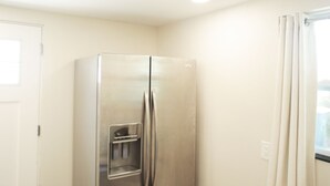 Eine kleine Küche mit einem Edelstahl-Kühlschrank, einer weißen Tür und einem Fenster mit Vorhängen.