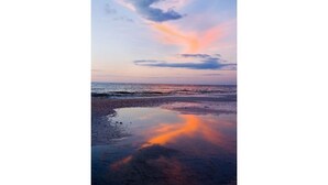 Ein Strand bei Sonnenuntergang mit ruhiger See und blauem Himmel.
