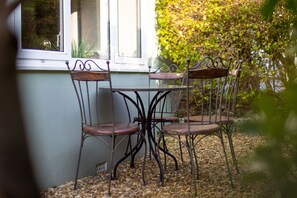 A table with four metal chairs and a window with a view of greenery. - Sunbury Villa - Close to Town and Beaches (Tenby)