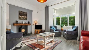 A cozy living room with a fireplace, comfortable seating, and a large window offering a view of greenery.