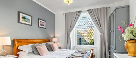 Un dormitorio con una cama de madera, una mesita de noche, una lámpara, una ventana con cortinas y vistas al exterior.