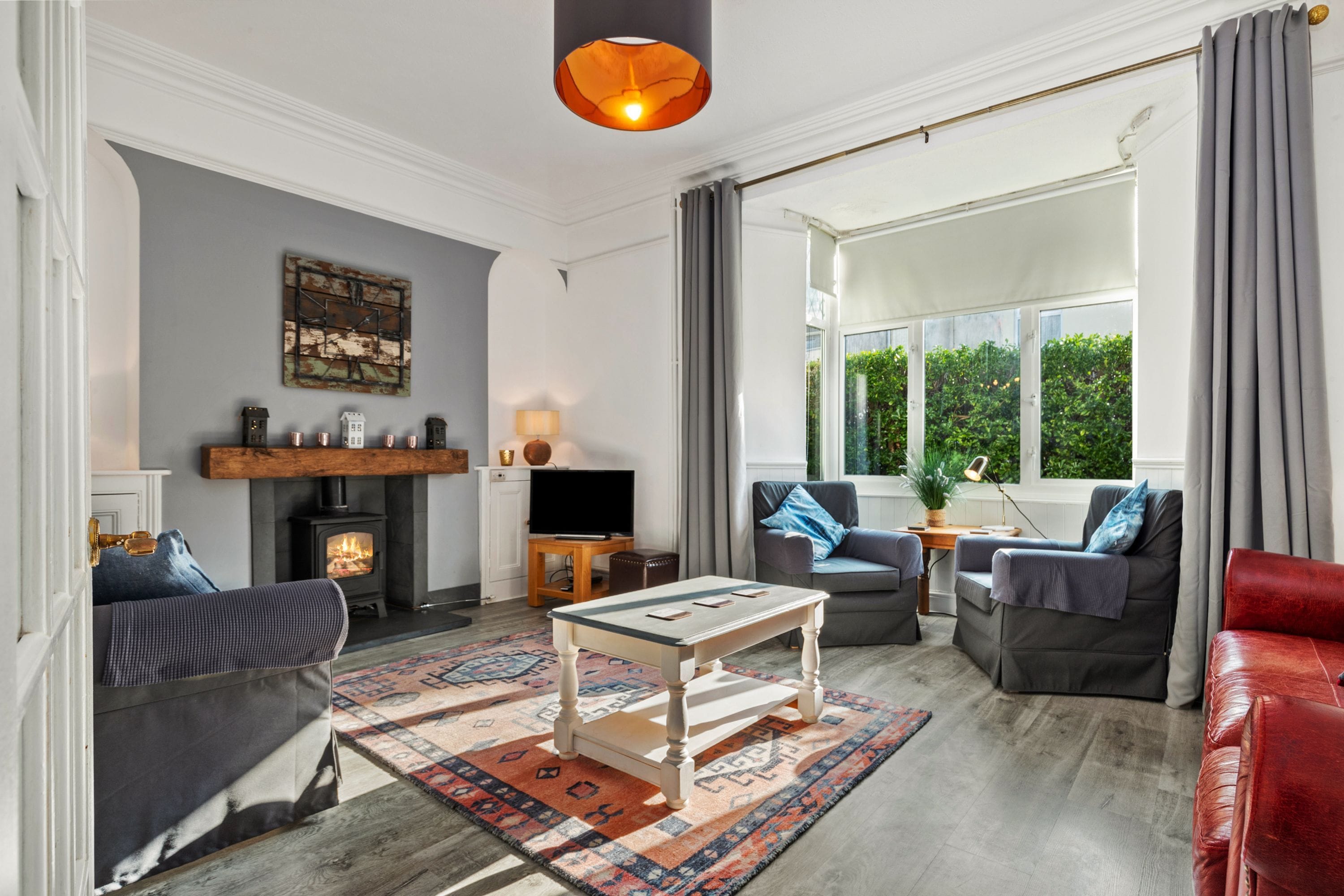 A cozy living room with a fireplace, comfortable seating, and a large window offering a view of greenery.