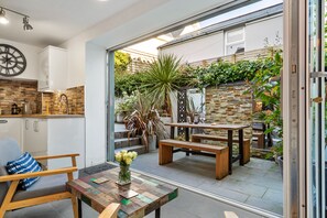 Eine moderne Küche mit einer Uhr, ein Essbereich mit Holzzmöbeln und ein Garten, der durch Glastüren sichtbar ist.