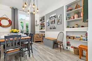 A dining area with a wooden table and chairs, a bench, and a bookshelf with various items. - Sunbury Villa - Close to Town and Beaches (Tenby)