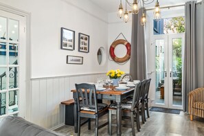 Un coin repas avec une table en bois dressée pour quatre personnes, entourée de chaises. Des tableaux encadrés ornent le mur, ainsi qu’un anneau décoratif et un vase rempli de fleurs jaunes.