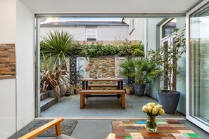 Un patio moderno con un banco de madera, una mesa pequeña y un jarrón de flores.