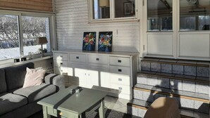 Et hyggeligt rum med træloft, en hvid murstensvæg, en sofa, et bord og et skab med skuffer.