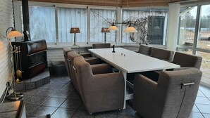 Et moderne spiseområde med et centralt bord, polstrede stole og hængende lamper.