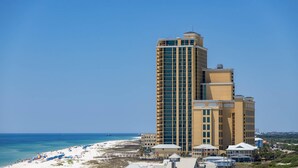 Un hotel alto con varios pisos, una playa en primer plano y un cielo azul despejado.