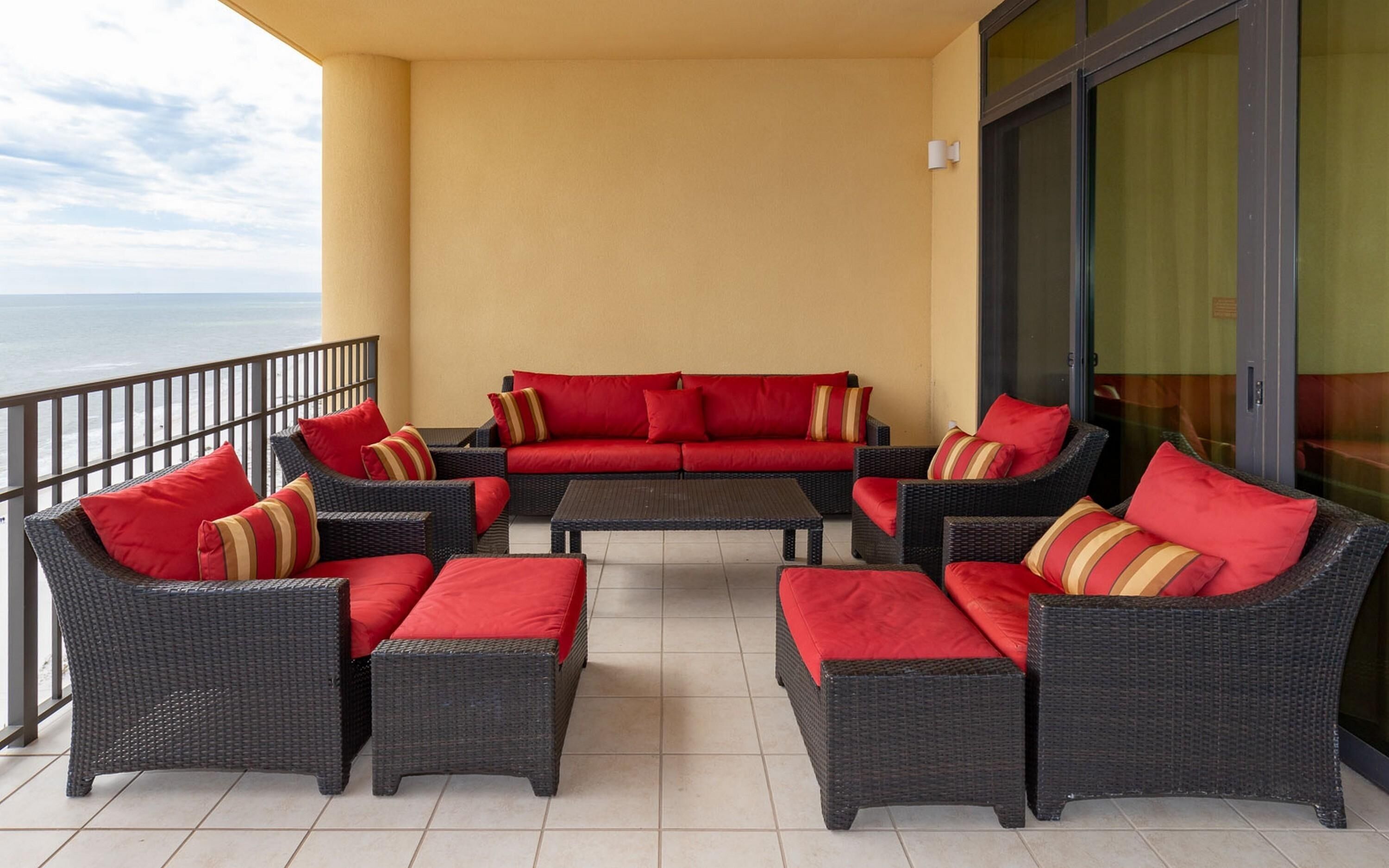 A balcony with wicker furniture, red cushions, and a view of the sea.