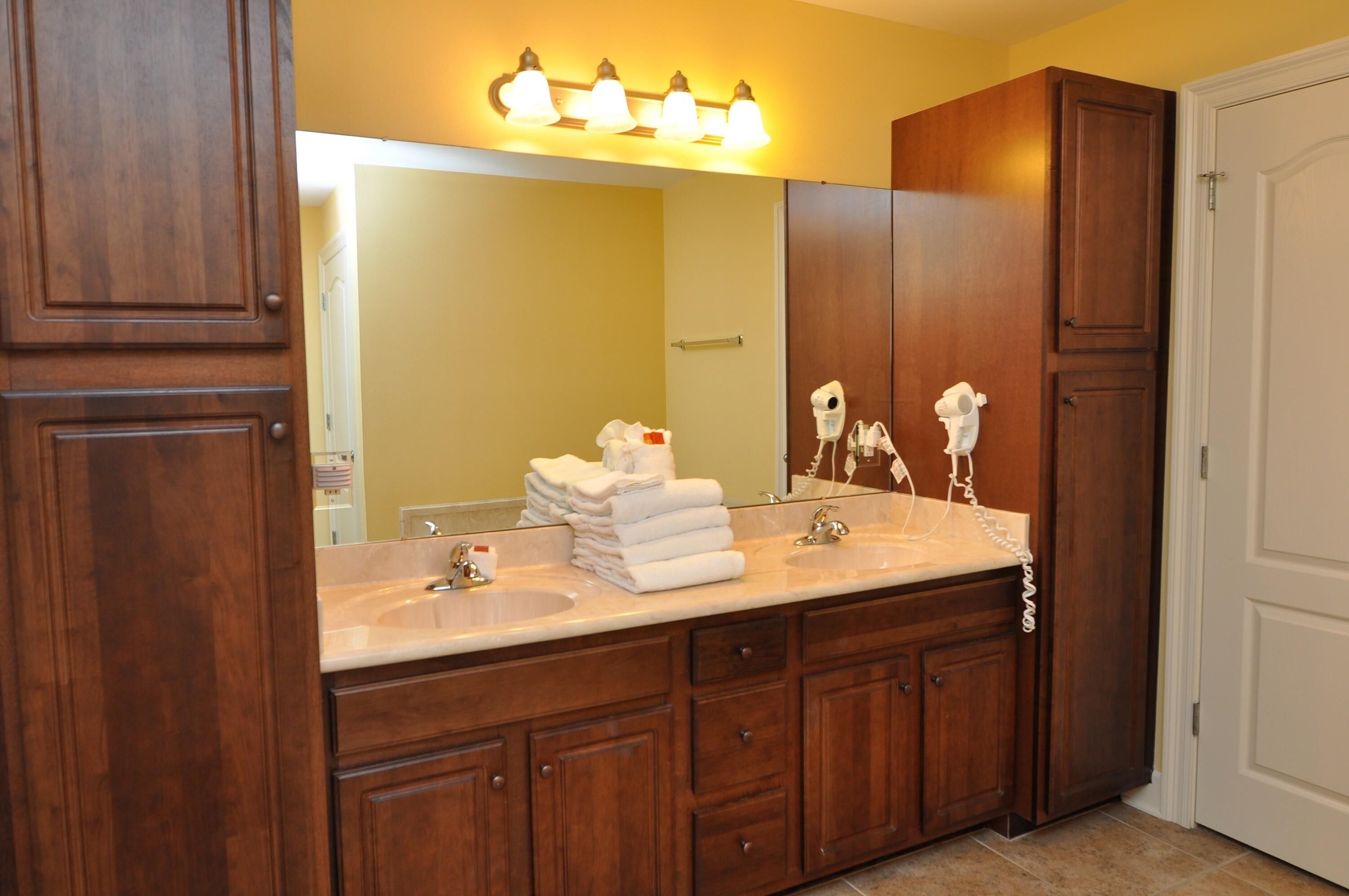 A bathroom with wooden cabinets, a double sink, and a mirror with lights above.