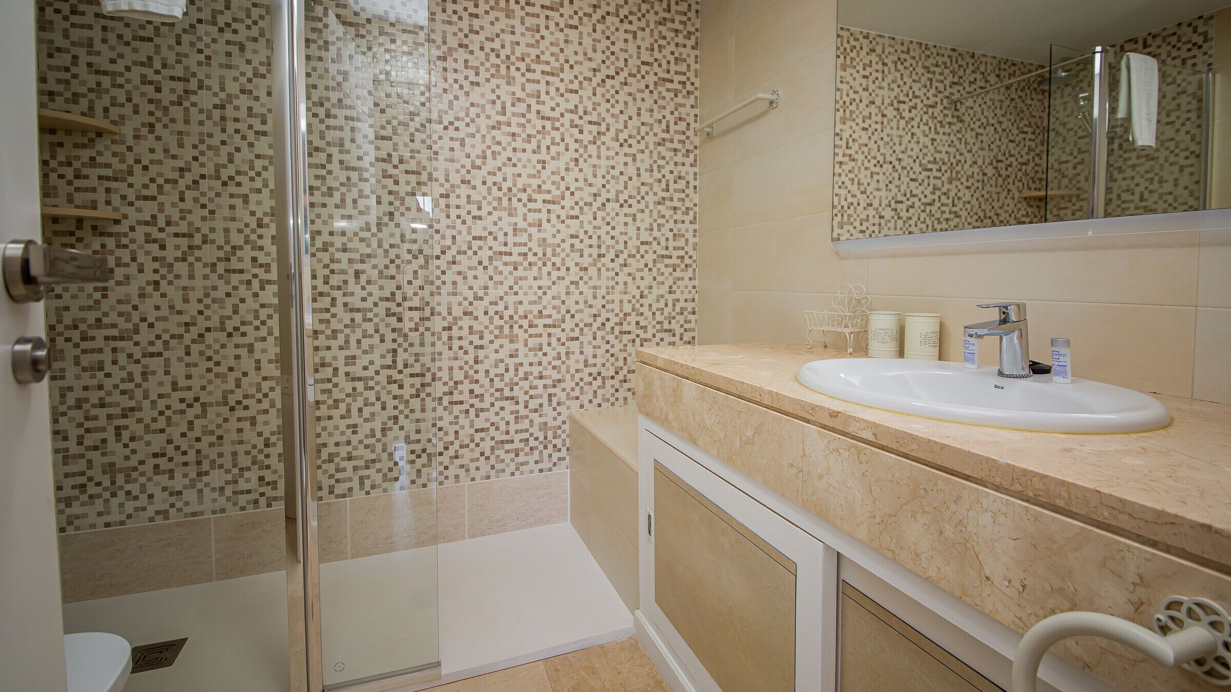 Un baño con cabina de ducha de vidrio, lavabo con artículos de aseo y espejo.