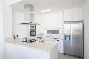 Cocina moderna con armarios blancos, electrodomésticos de acero inoxidable y una isla central con un cuenco de fruta.