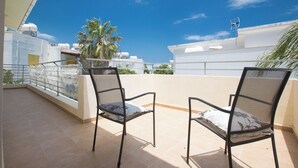 Twee zwarte metalen stoelen op een betegeld balkon, met een helderblauwe lucht en gebouwen op de achtergrond.