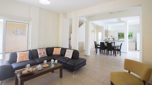 Een moderne woonkamer met een donkere bank, salontafel en een gele fauteuil. Op de achtergrond is een eethoek met een tafel en stoelen zichtbaar.