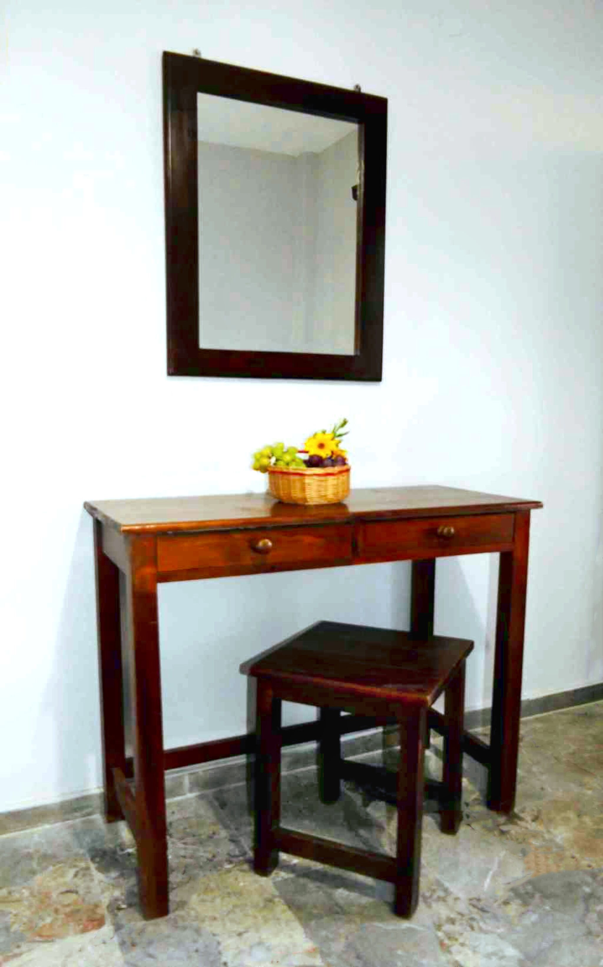 A wooden desk with a mirror above it and a small stool in front.