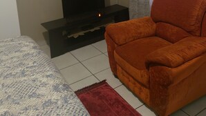 Una sala de estar con un televisor sobre un soporte negro, un sofá rojo, un lecho estampado y una alfombra roja.