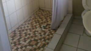 Un baño con ducha, inodoro y suelo de baldosas.
