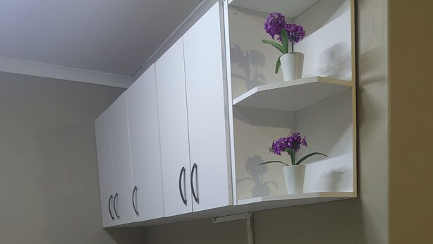 Una cocina con armarios blancos, un microondas, una estufa a gas y un estante con flores moradas.