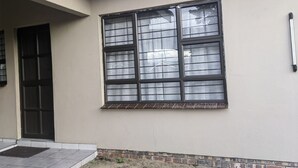 Fachada de edificio con un ventanal grande, una puerta y un pequeño espacio exterior con suelo de baldosas.