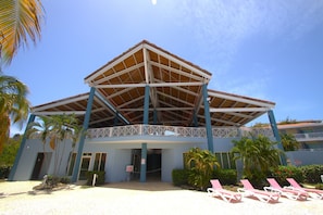 A building with a covered entrance, palm trees, and beach chairs. - Costa Bonita Private Villa 604 (Culebra)