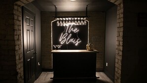 Ein schwach beleuchteter Korridor mit einem Neonzeichen, auf dem 'The Blais' steht, über einem Barbereich.