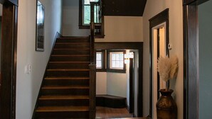 Eine Holztreppe führt zu einer oberen Etage, auf dem Boden steht eine Vase mit Trockenpflanzen und eine Tür mit einem Lichtschalter.