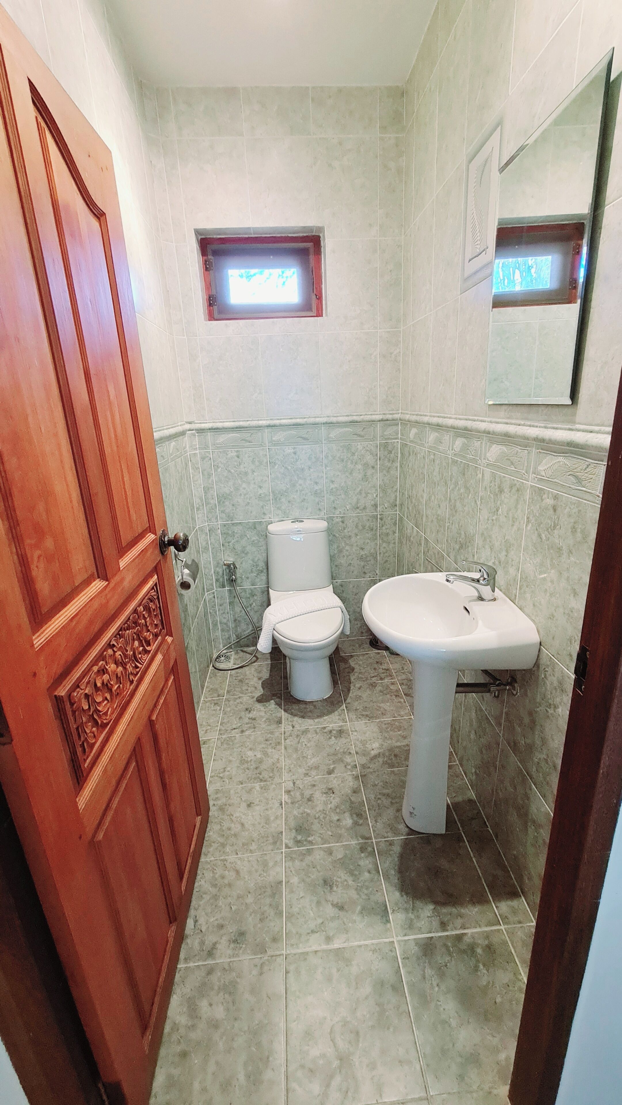 Ein Badezimmer mit Holztür, Toilette, Waschbecken und kleinem Fenster.