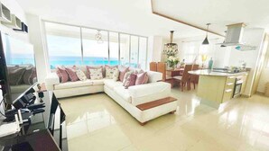 A modern living room with a white sectional sofa, a dining area, and a kitchen. - 3 Bedrooms At Marbella Beachfront Juan Dolio No820 (Guayacanes)