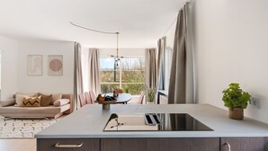 A modern kitchen with a central island, a dining area with chairs, a sofa, and a view of the outdoors. - Charm 1 - Chic 2-bdr Apt With Shared Garden (Copenhagen)