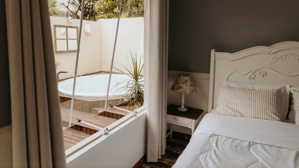 A bedroom with a bed, a nightstand, a lamp, and a view of a hot tub and outdoor area. - Paty's Garden (Florianópolis)