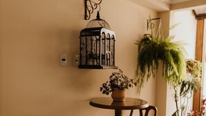 A small, round wooden table with two chairs, a potted plant on the table, and a hanging birdcage on the wall. - Paty's Garden (Florianópolis)