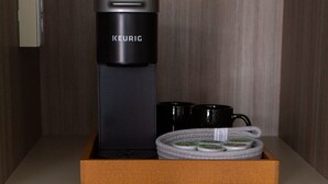 Una cafetera Keurig, dos tazas negras y un hervidor enrollado dentro de una caja de madera.